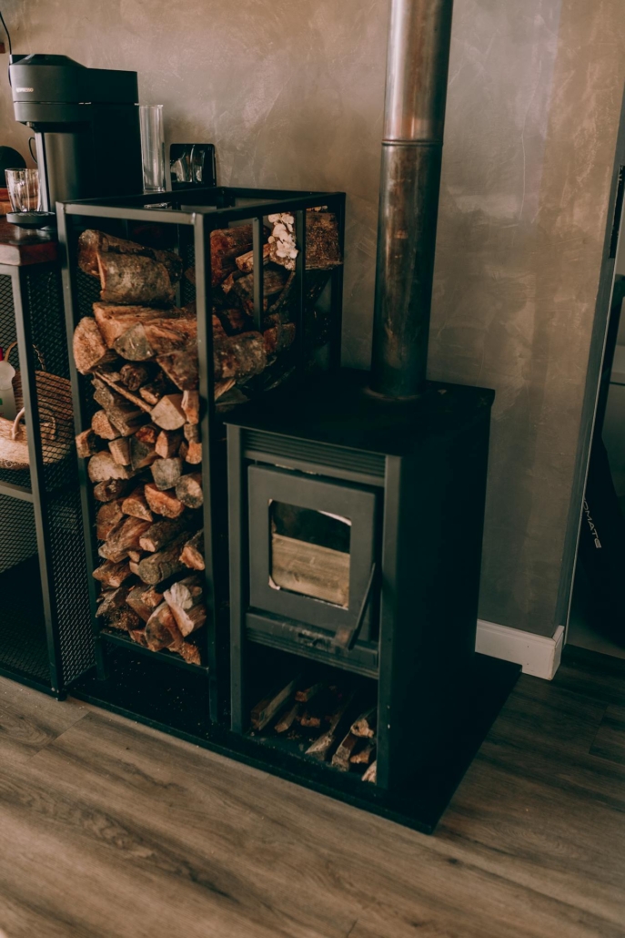 Een houtkachel met een rek vol haardhout ernaast, klaar voor gebruik tijdens de wintermaanden.