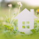 Papieren huis omringd door groen gras en bloemen, symbool voor duurzaam wonen en milieuvriendelijke maatregelen.